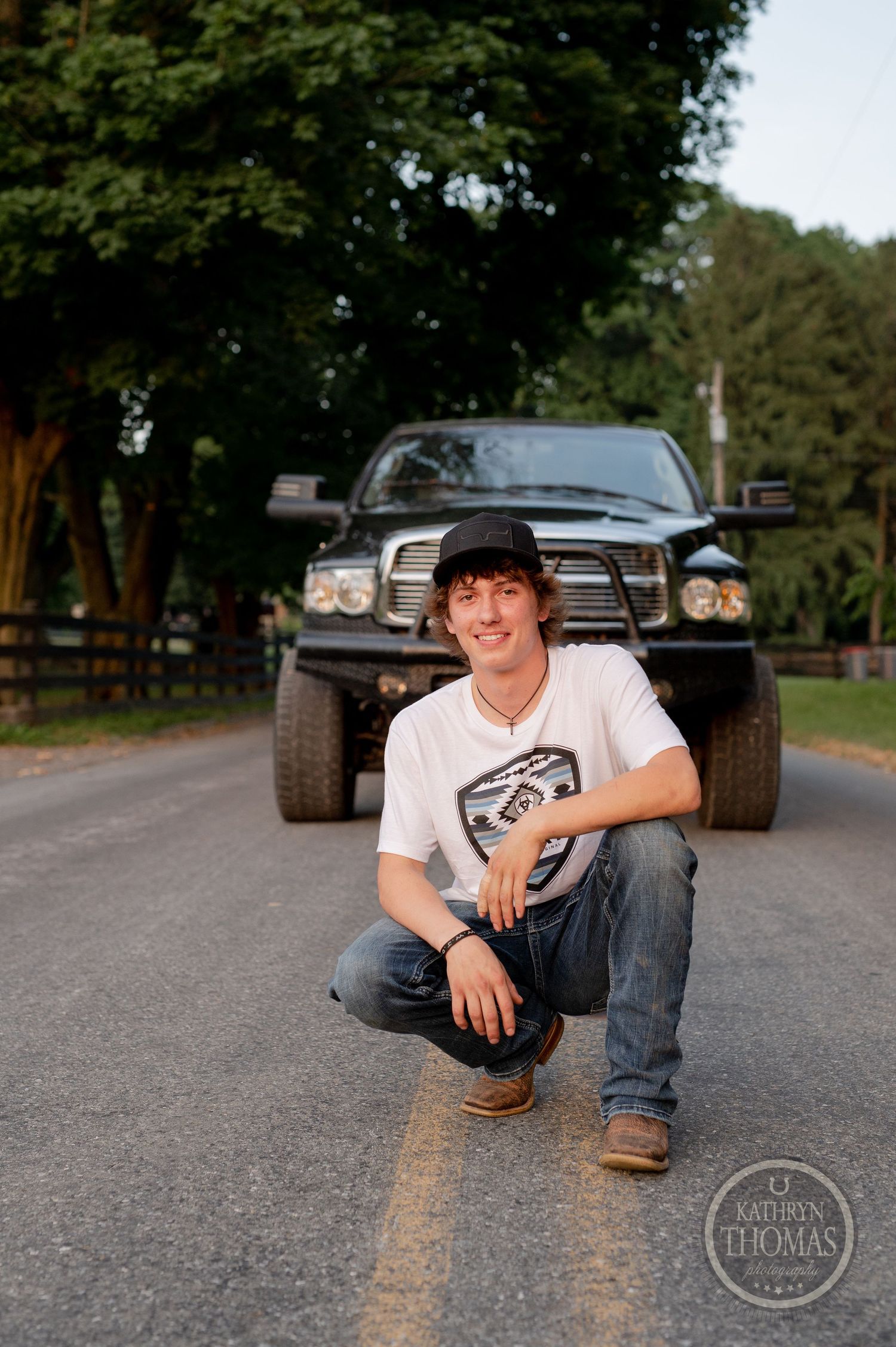 Black Dodge Ram with custom suspension photographed on tree-lined country road.