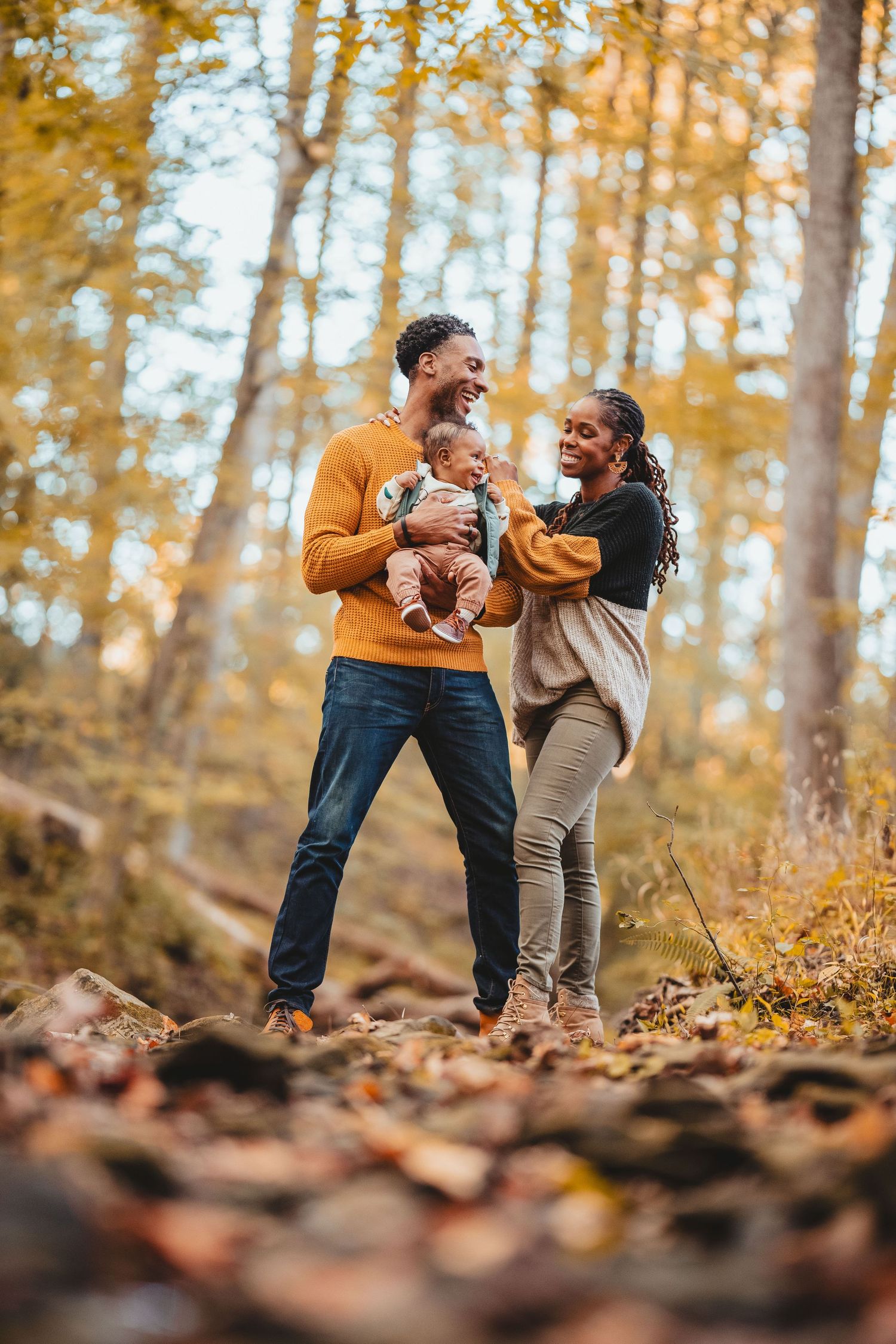 A family enjoying a warm autumn day together in a forest filled with golden fall foliage and fallen leaves.
