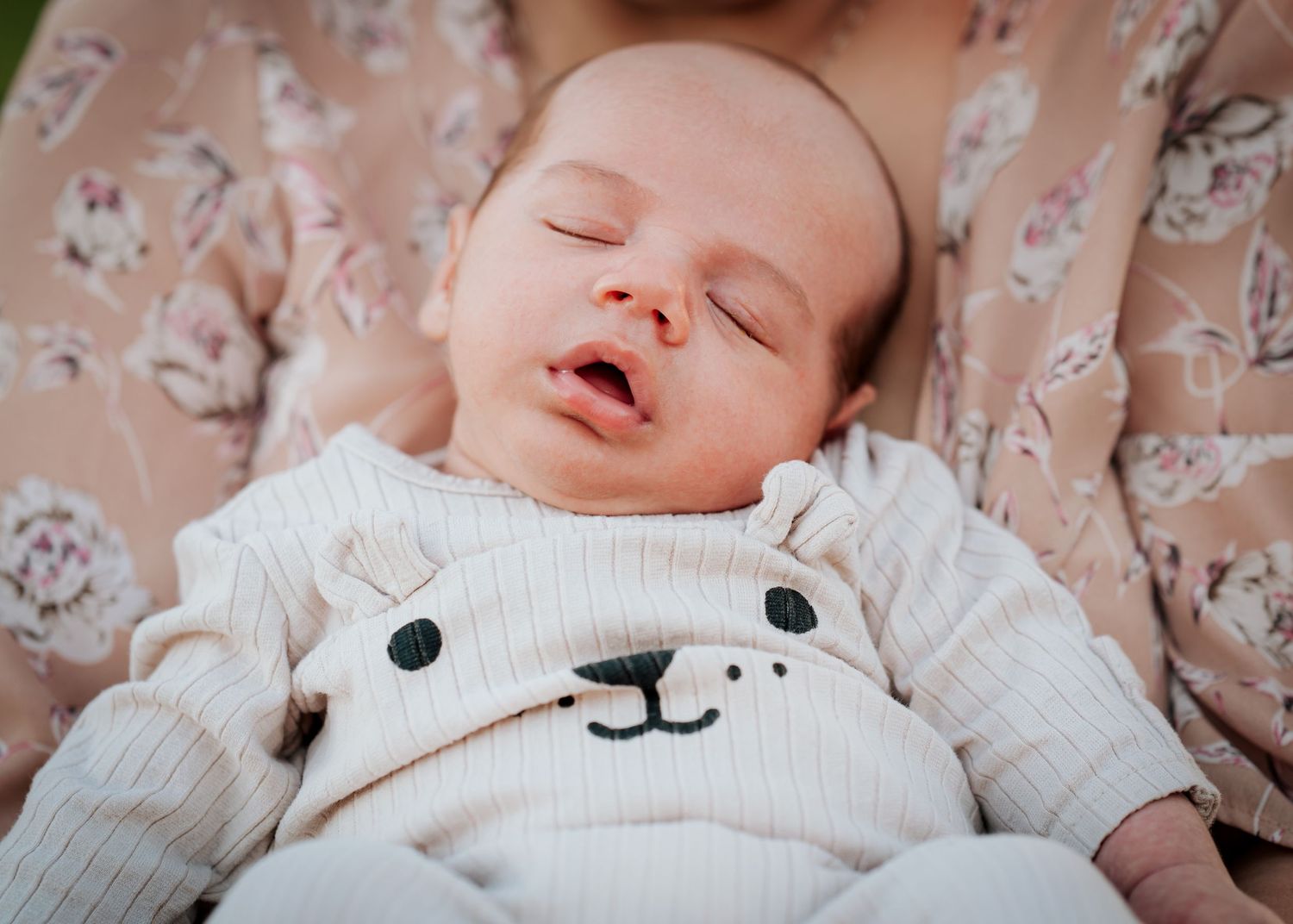 Sleeping baby wearing white bear sweater smiles contentedly during nap.