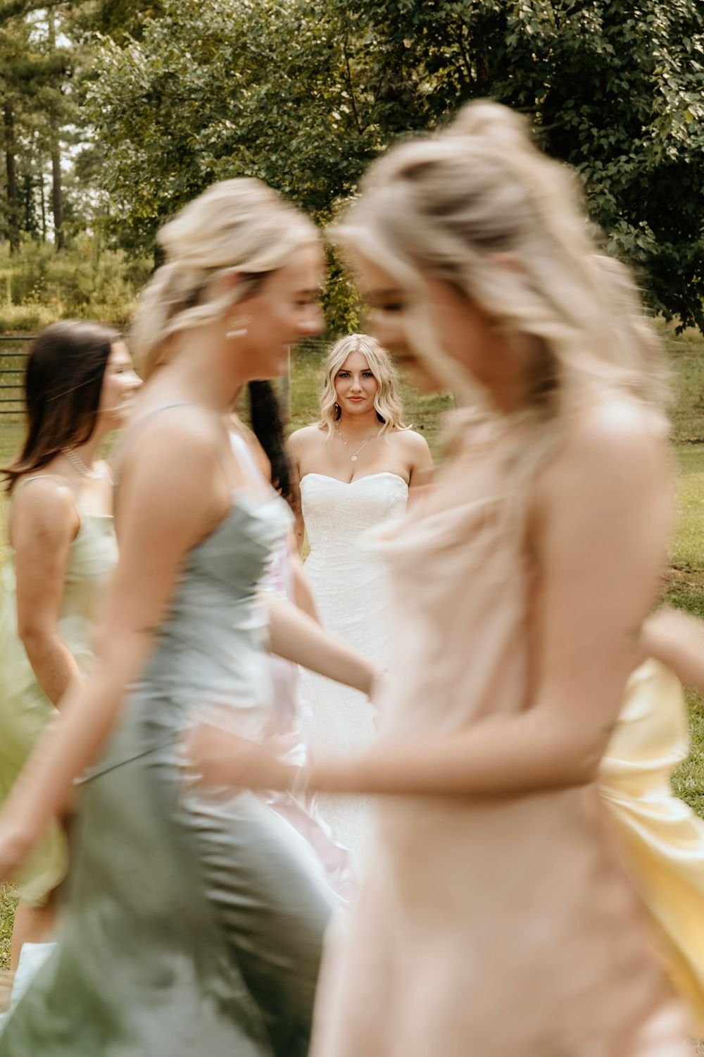 Elegant wedding party members in pastel dresses share a candid moment outdoors during a summer celebration.