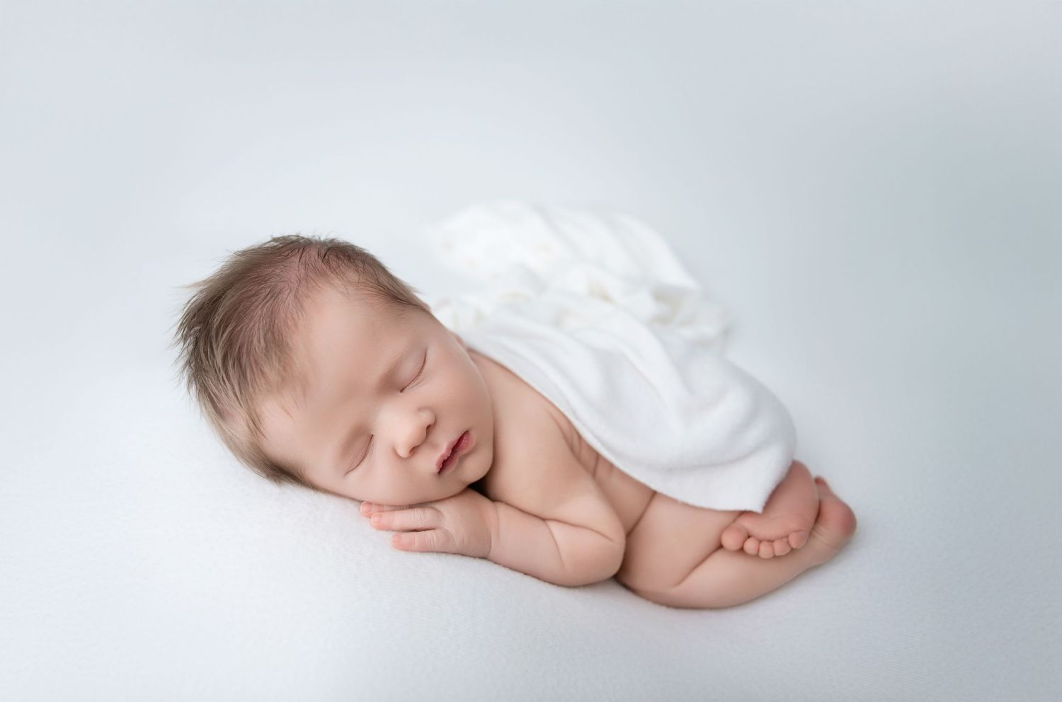 Peaceful sleeping newborn baby wrapped in soft white cloth lying on light background. Hanford Newborn Photographer