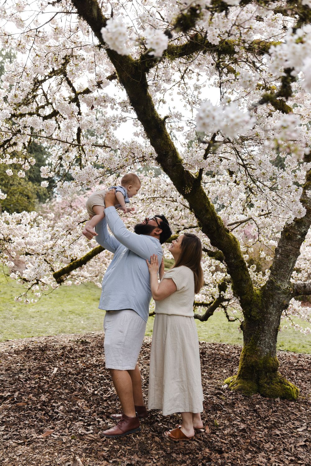 A tender moment captured under blooming cherry blossom trees in a spring garden setting.