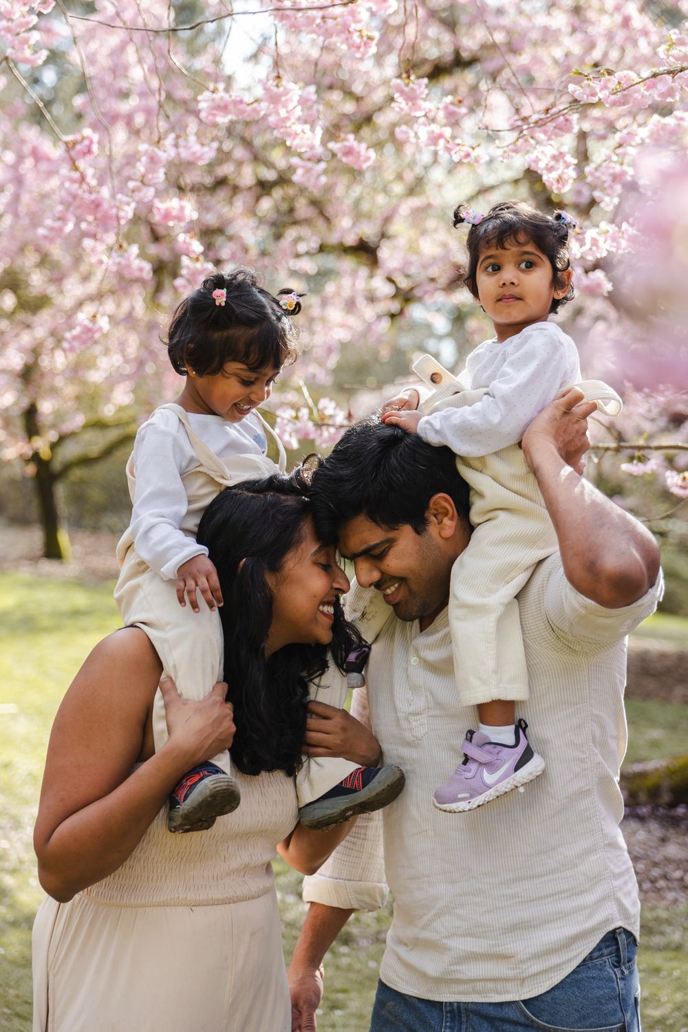 Family in white outfits sharing tender moments under blooming cherry blossom trees in a spring photo series.