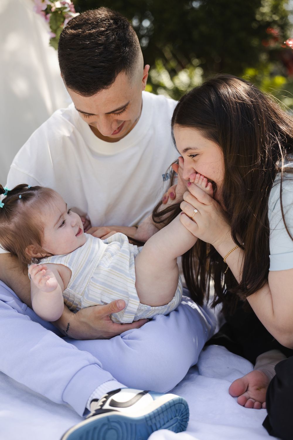 A joyful family moment outdoors as they share laughter while sitting together on a blanket in natural lighting.
