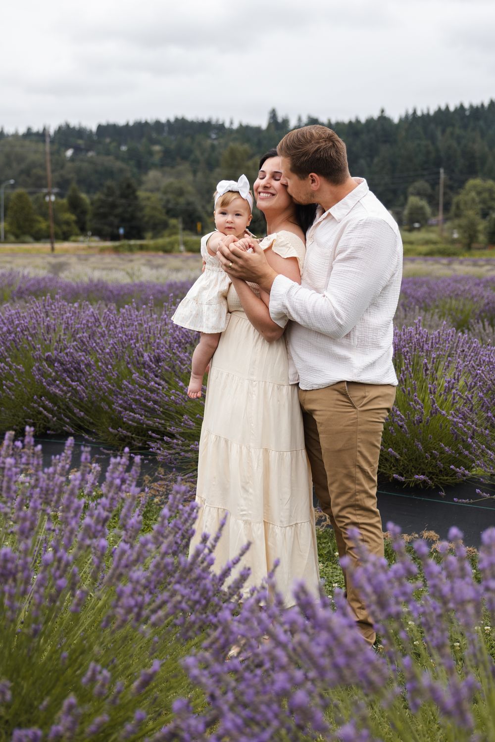 Family shares tender moment together in a blooming lavender field with evergreen forest in background.