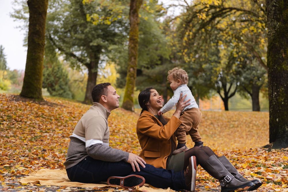 Family lying together on autumn leaves in a park during a fall photoshoot with golden foliage all around.