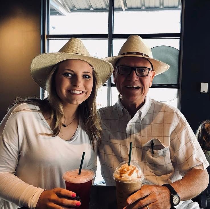 Two people wearing cowboy hats smile while holding cold beverages inside a restaurant or cafe.