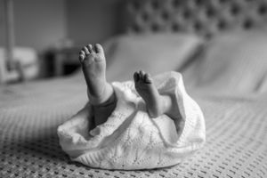 Black and white image of baby feet peeking out from white blanket.
