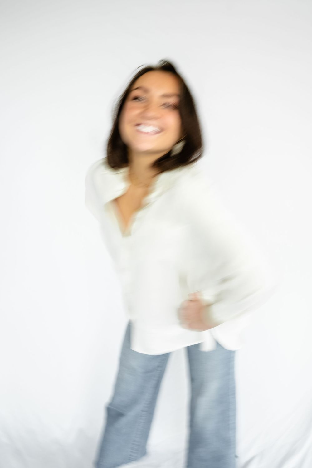 Motion-blur portrait in white shirt and jeans against studio backdrop.