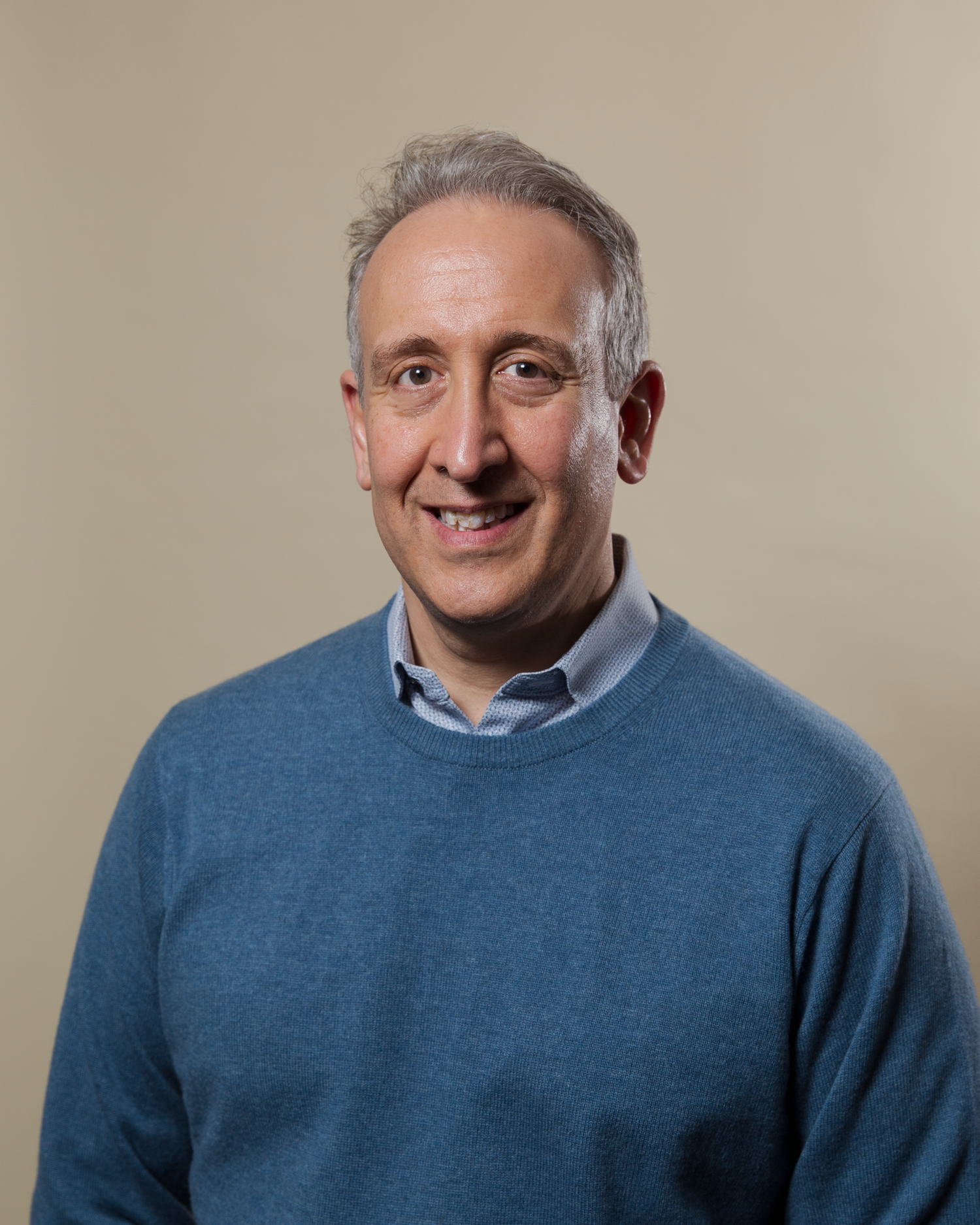 Professional headshot portrait of someone wearing a light blue sweater and collared shirt against a neutral backdrop.