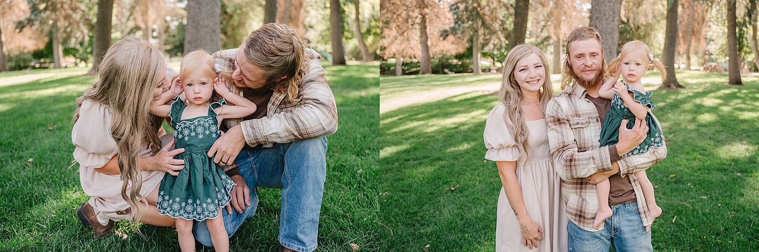 Family in casual clothing embraces while standing together on green grass in a peaceful wooded park setting.