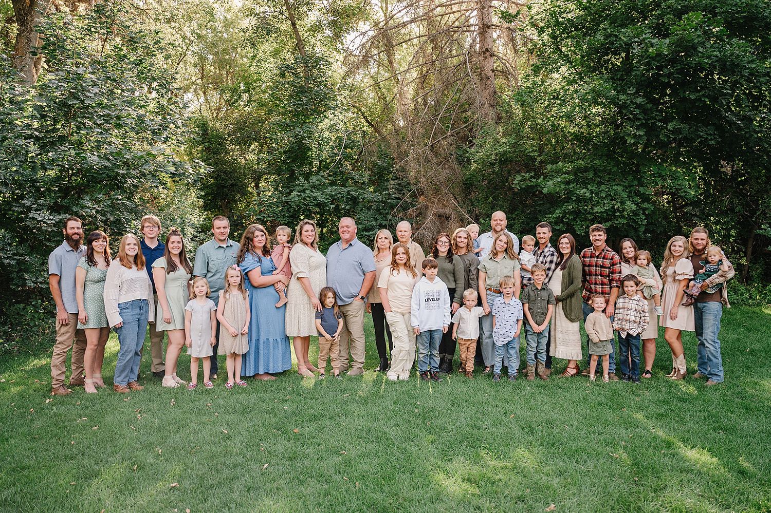 Large family group dressed in coordinating pastel blue and white outfits poses together on green lawn for outdoor portrait.