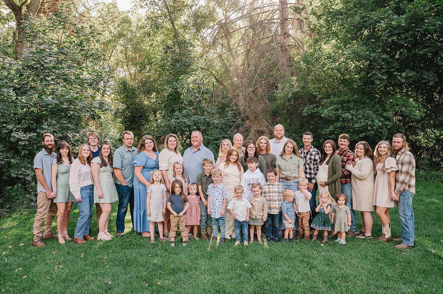 Group photo of people in coordinated blue and neutral tones standing together outdoors on grass with greenery in background.