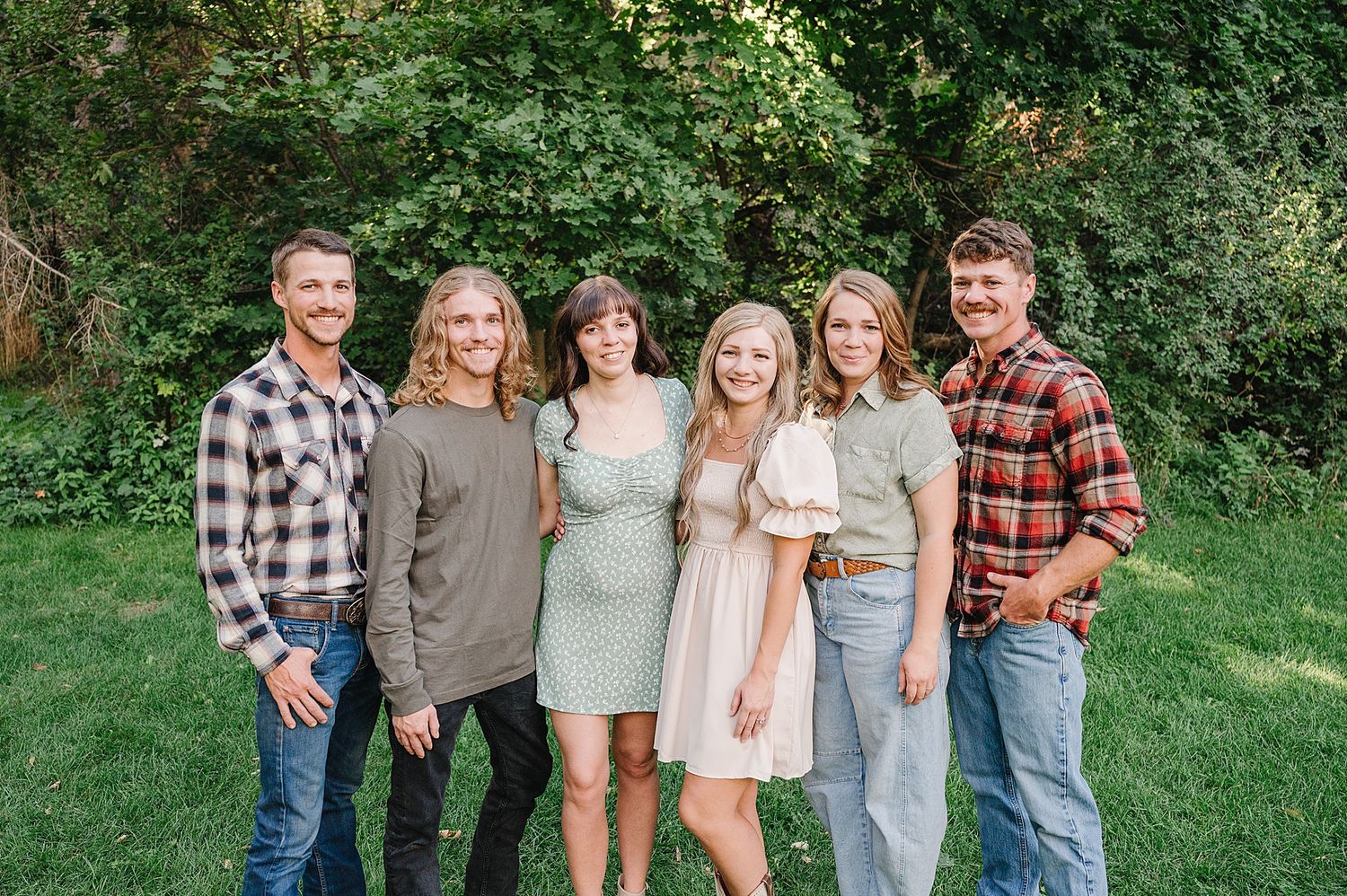 Small group portrait in casual attire with plaid shirts and neutral colors standing together on a grassy lawn.