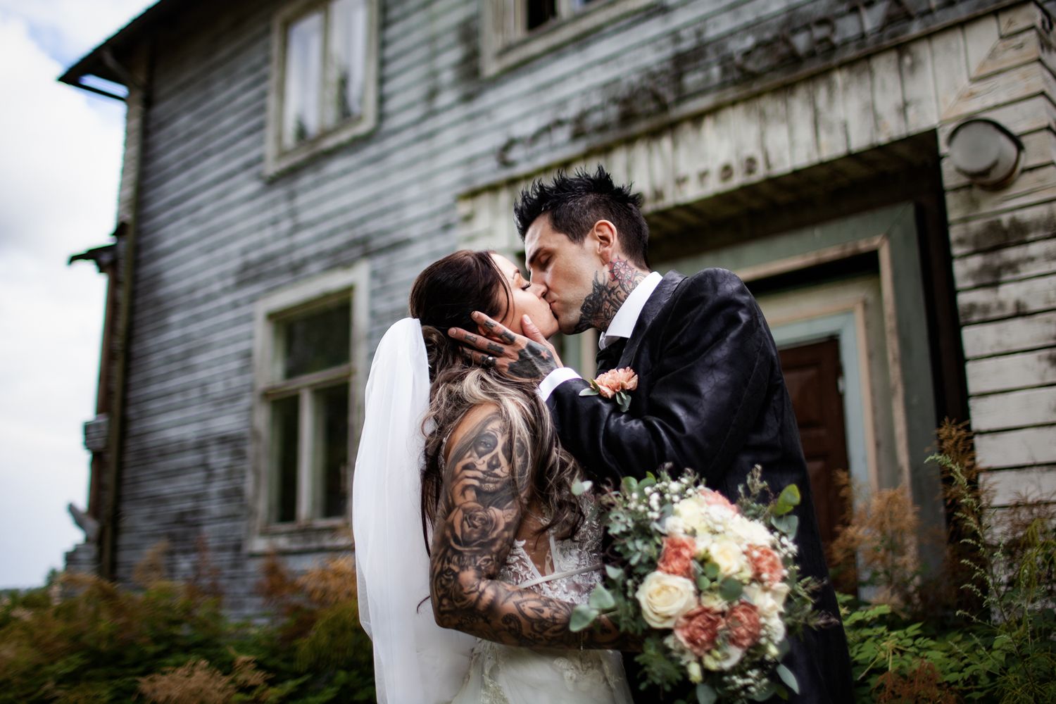 Couple sharing intimate moment in front of weathered white building during wedding shoot.