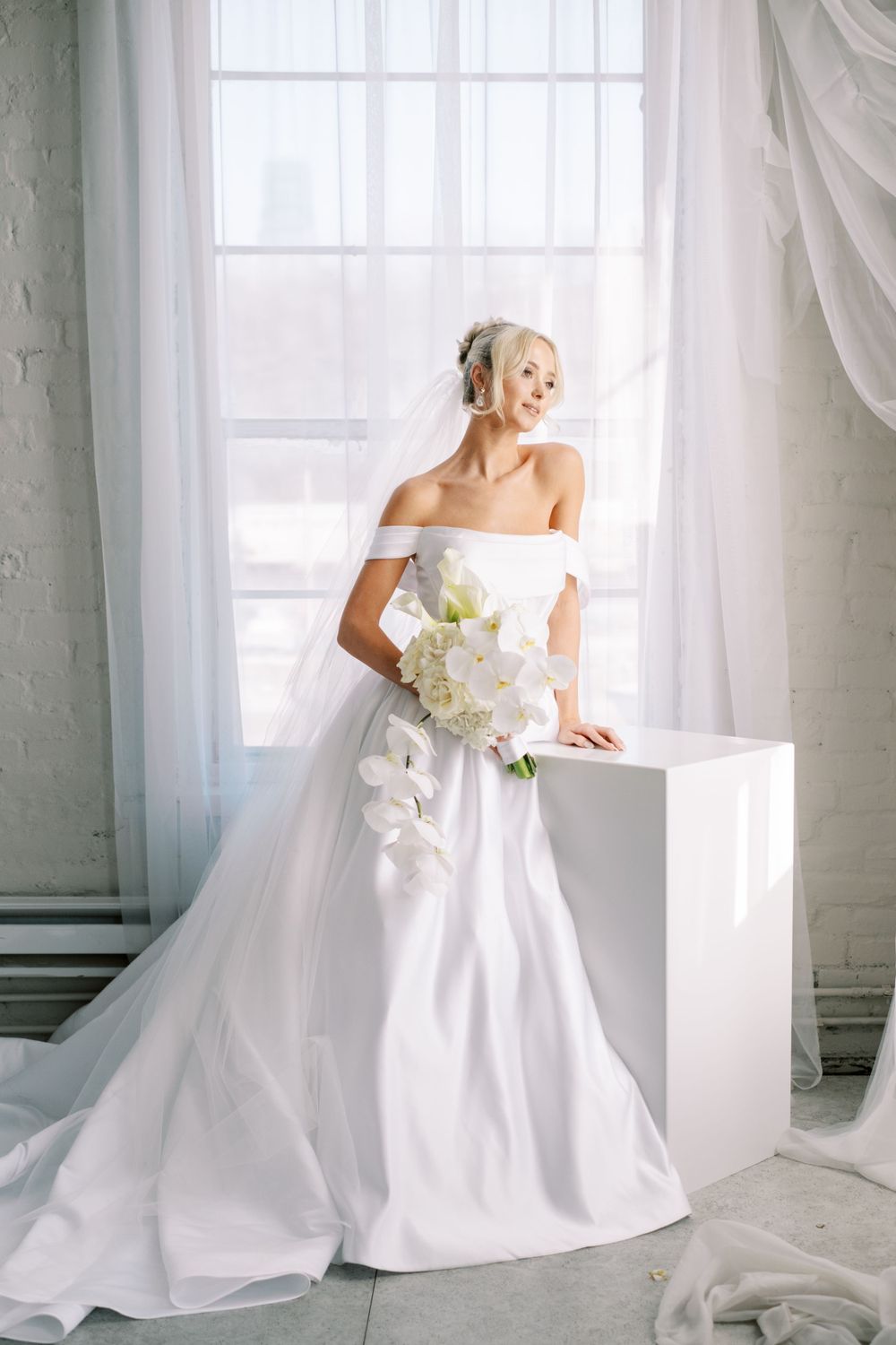 Classic bridal portrait session with white wedding gown and orchid bouquet near sunlit windows.