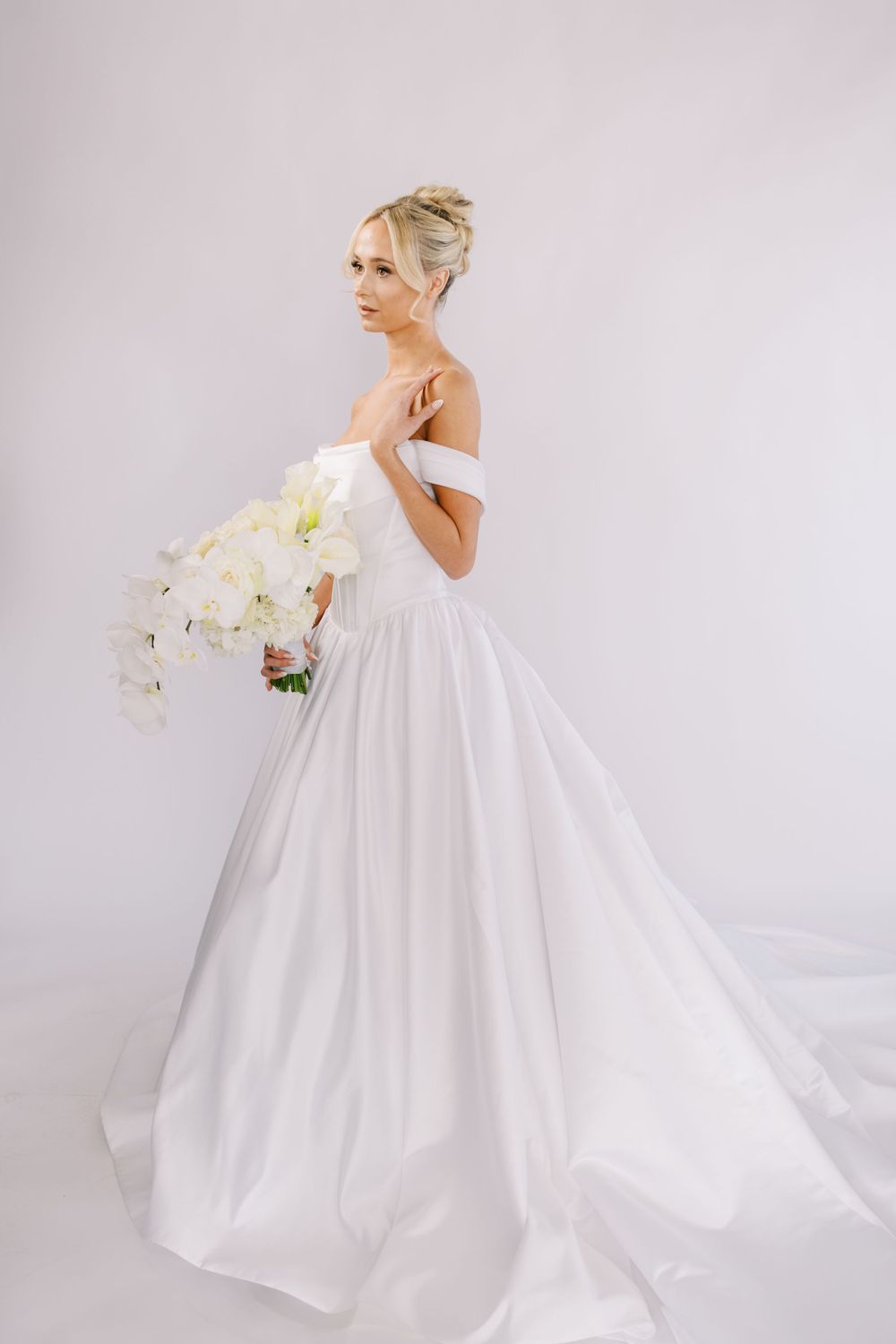 Dramatic full-length view of billowing wedding gown with orchid bouquet.
