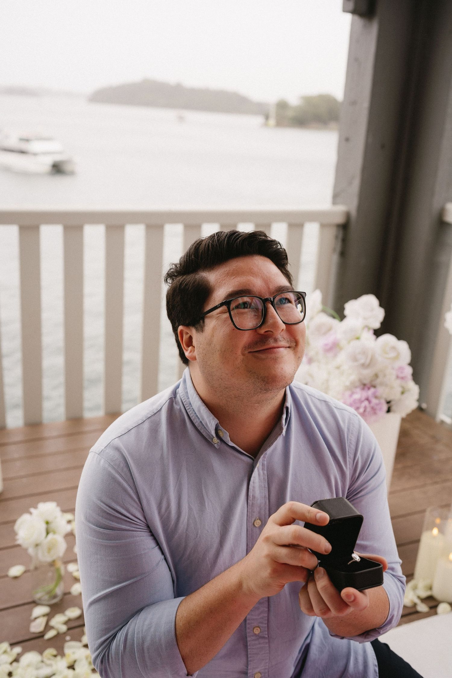 A romantic proposal moment with a ring box on a waterfront balcony with floral decorations.