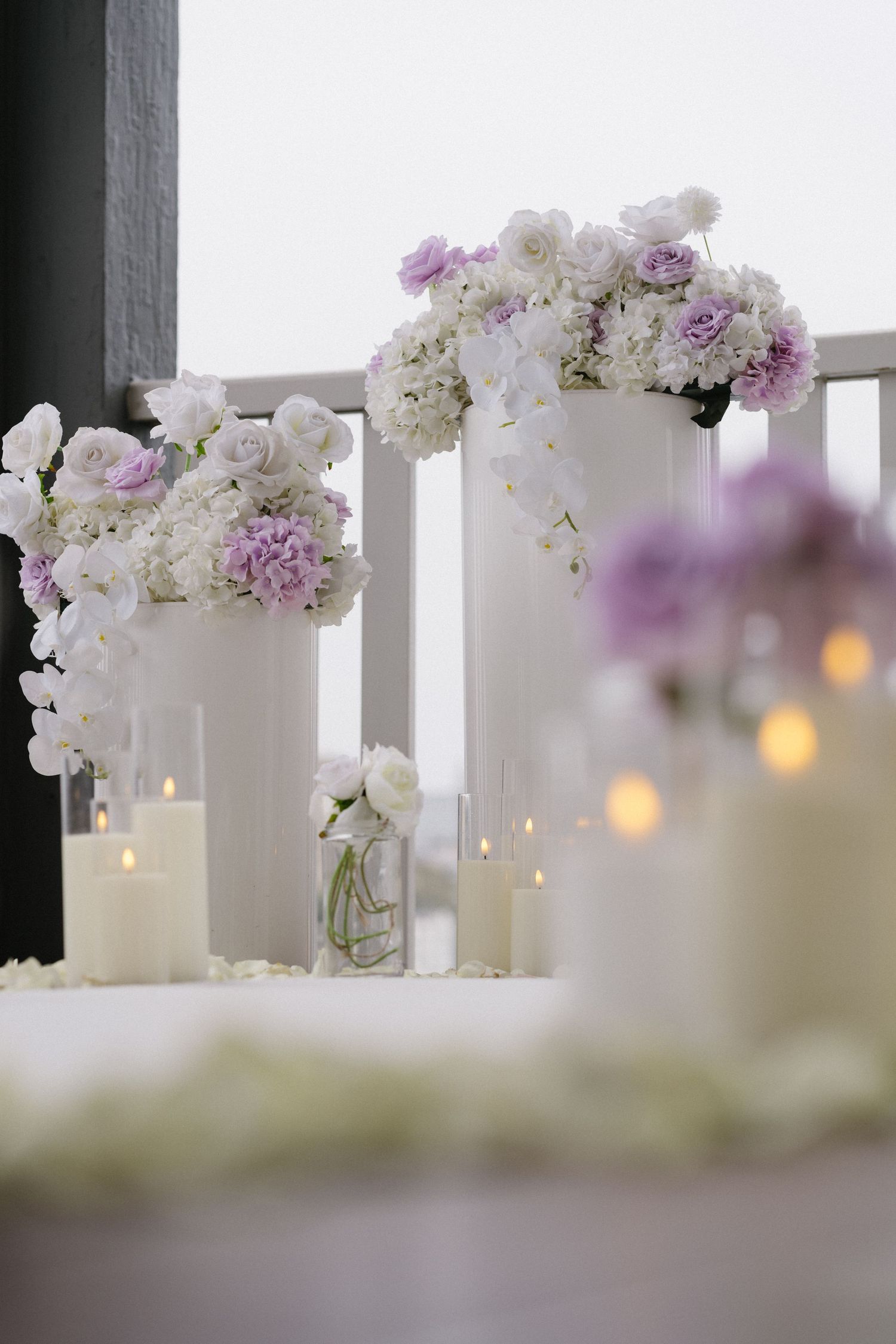 Elegant white and purple flower arrangements with glowing candles on a balcony railing.