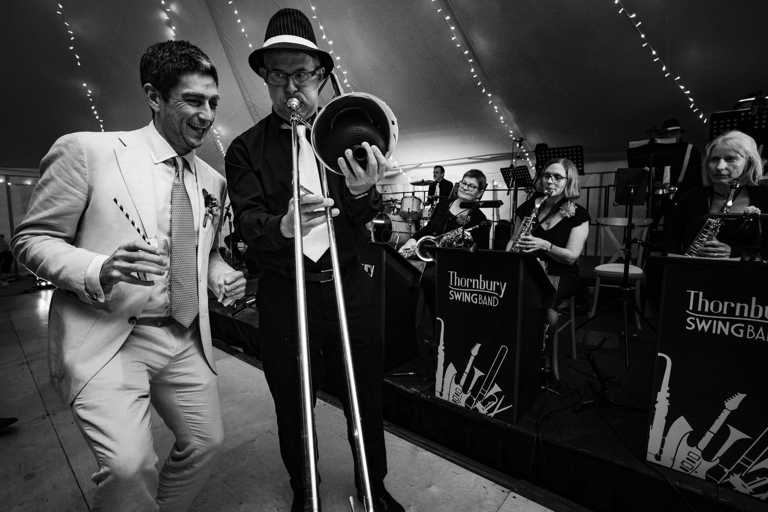 Two jazz musicians from Nova Scotia perform on stage in black and white holding a microphone with wedding guests.