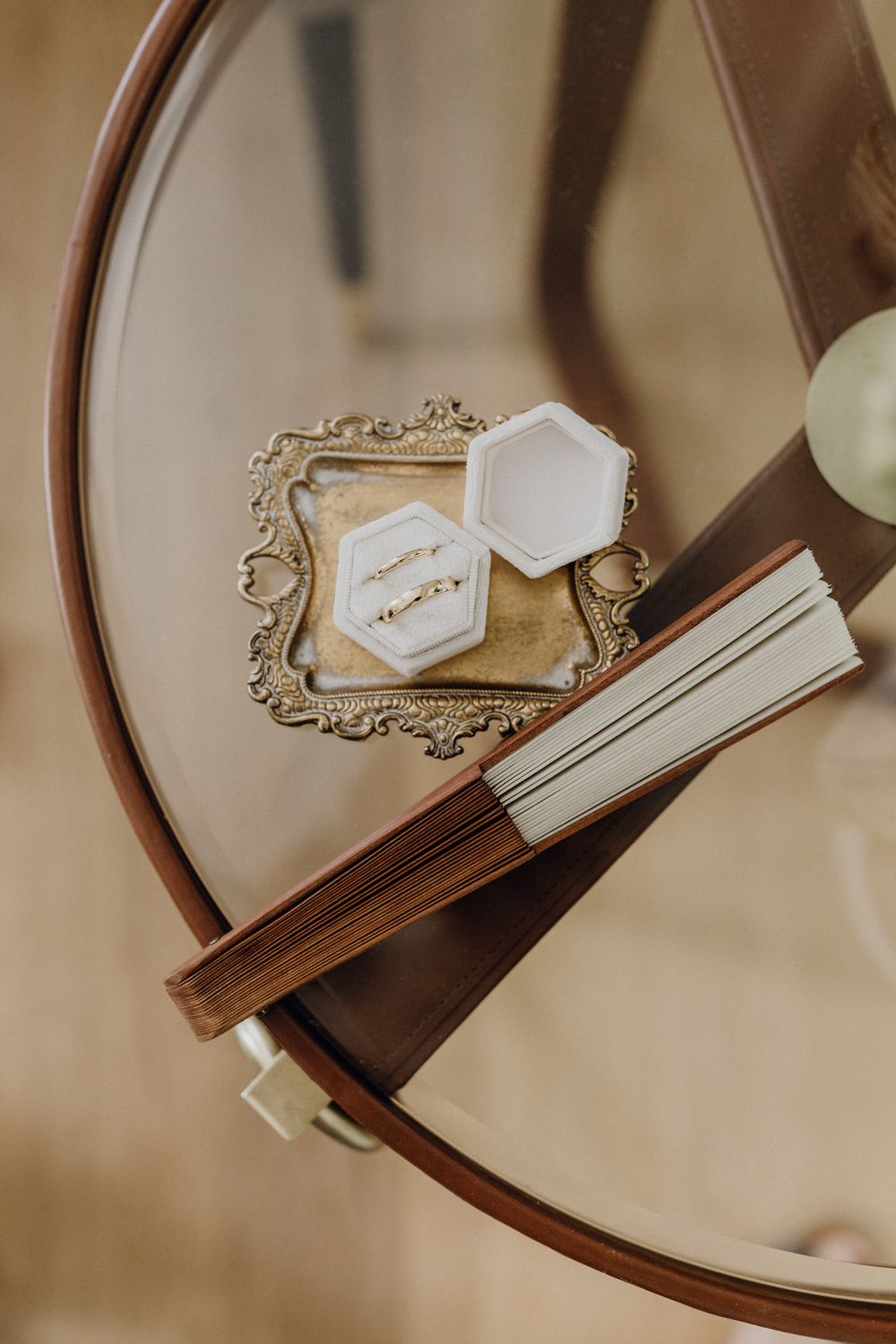 Hochzeitsringe schön dekoriert in einer Ringschachtel auf einem Goldtablett, rechts danaben liegt ein Holzfächer