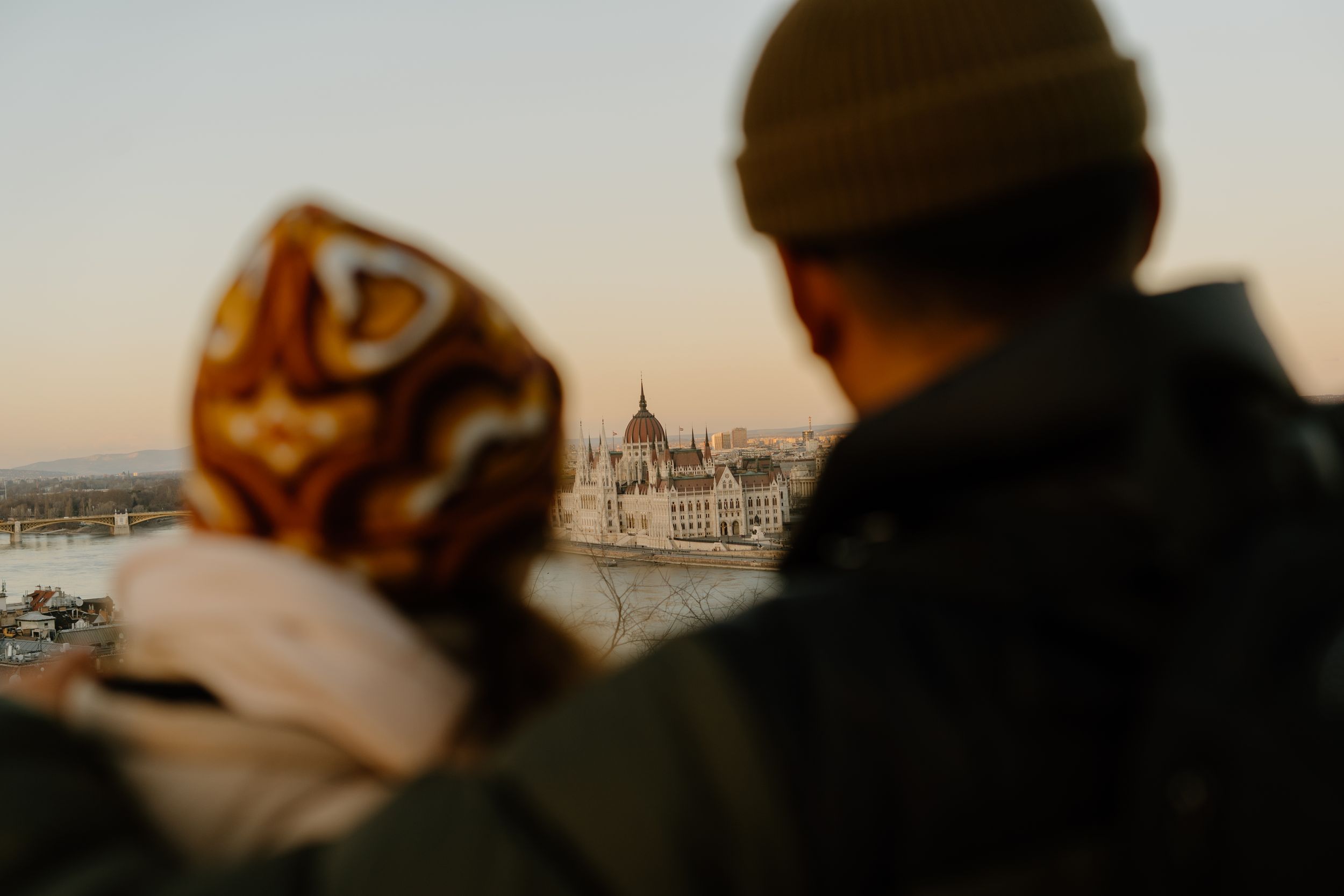Two people overlooking the Hungarian Parliament Building from a viewpoint along the Danube River in Budapest.