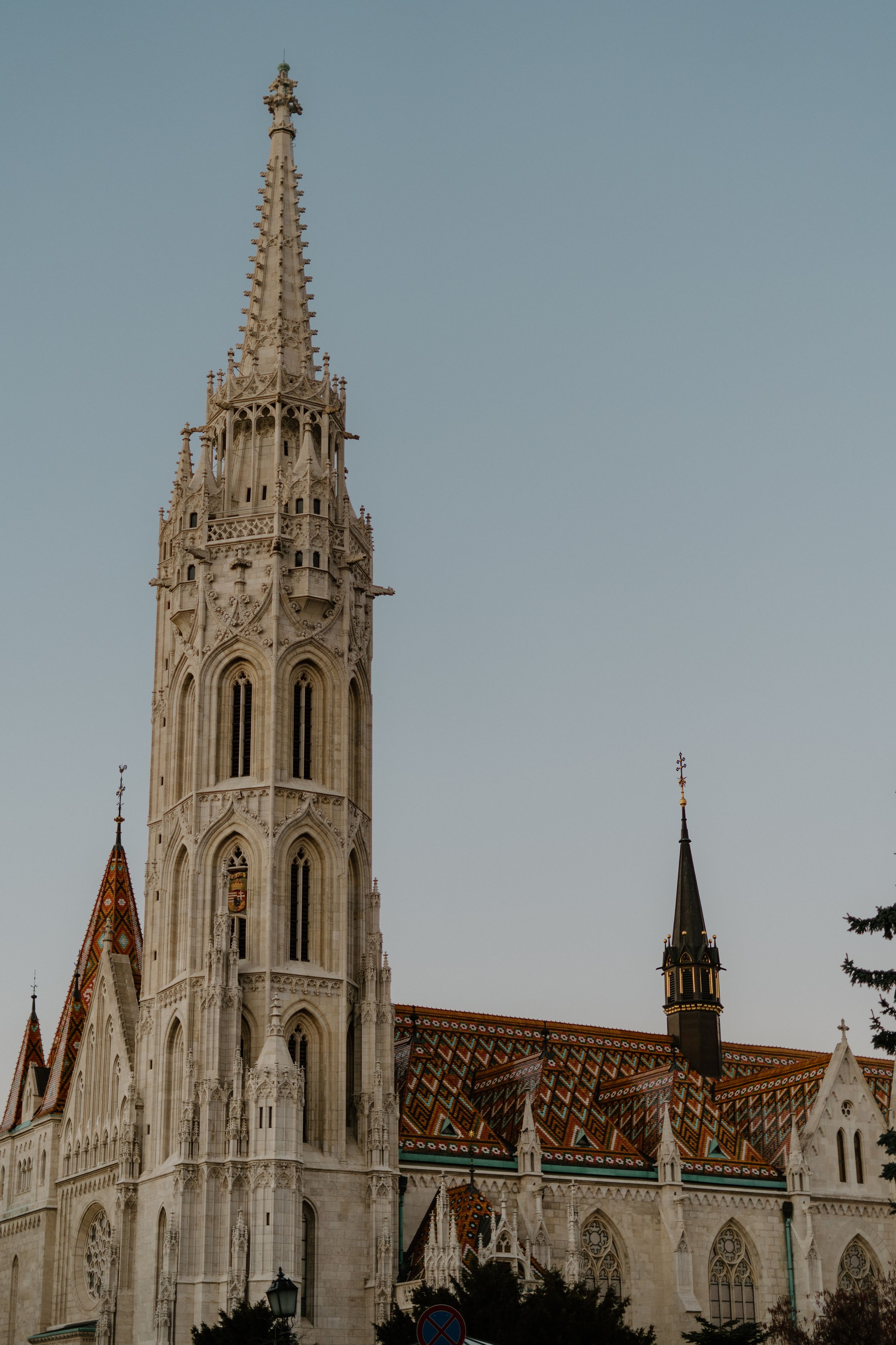 Ornate spire of the Matthias Church in Budapest featuring Gothic architecture against a pale blue sky.