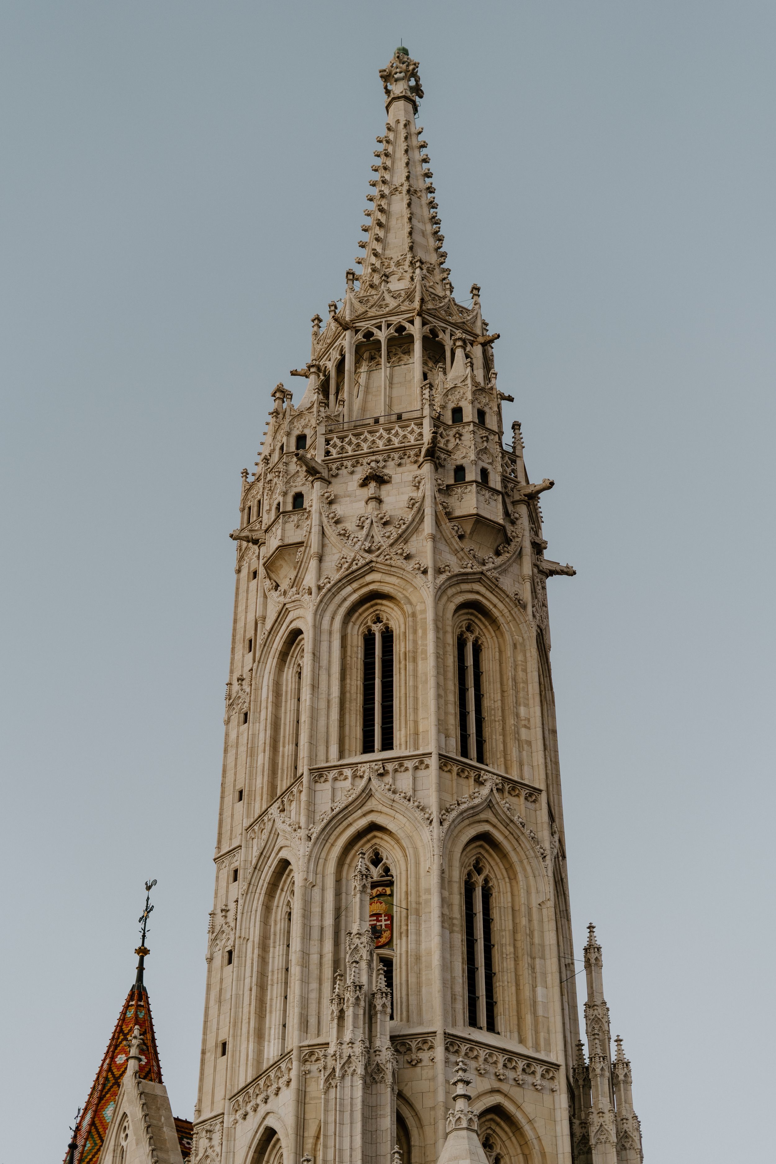 A Gothic church spire with detailed architectural ornaments and pointed arches rises against a grey sky.