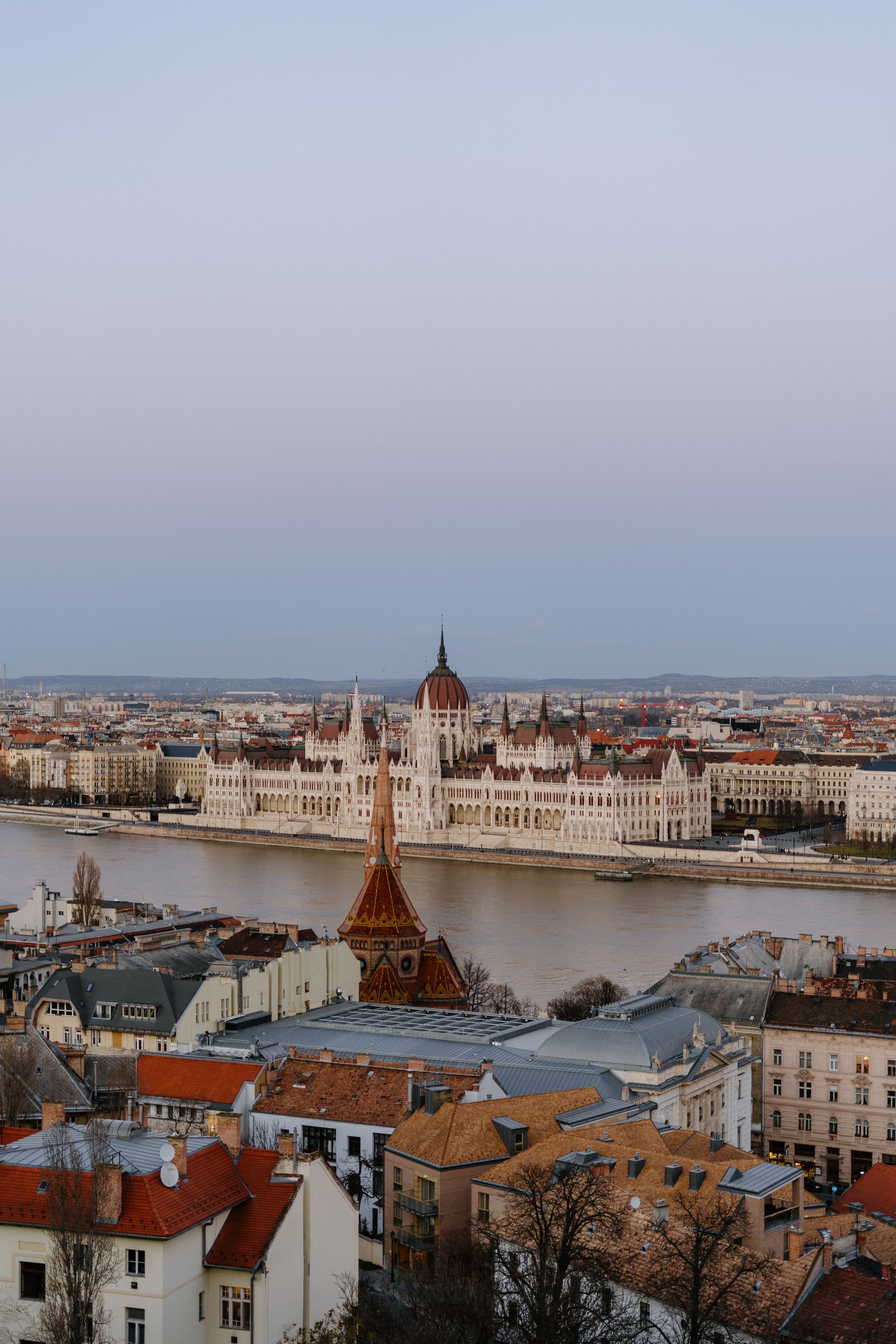 Aerial view of Budapest's iconic Parliament Building along the Danube River with historic cityscape at sunset.