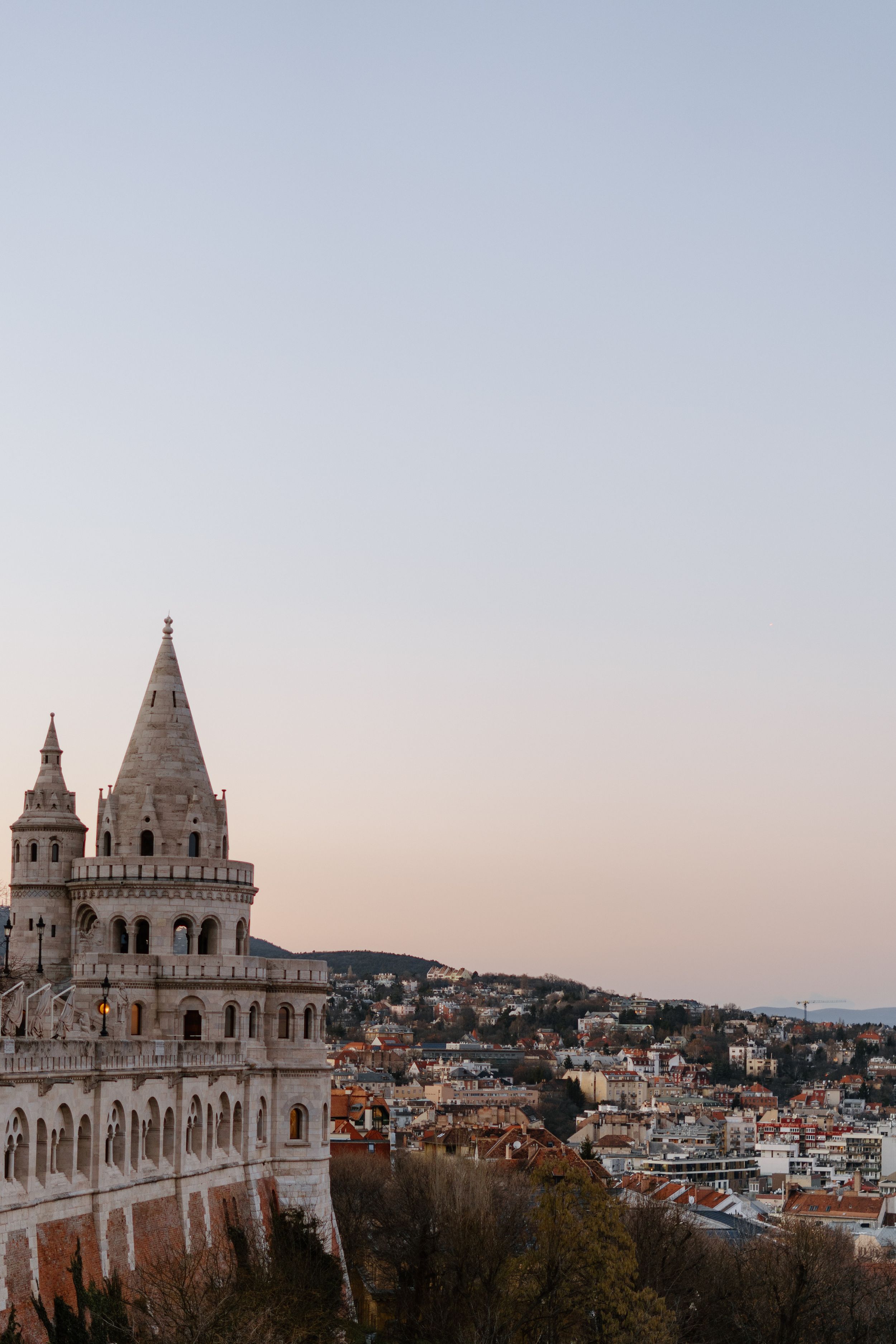 Fisherman's Bastion towers rise above Budapest's cityscape during sunset, offering panoramic views of the historic city.