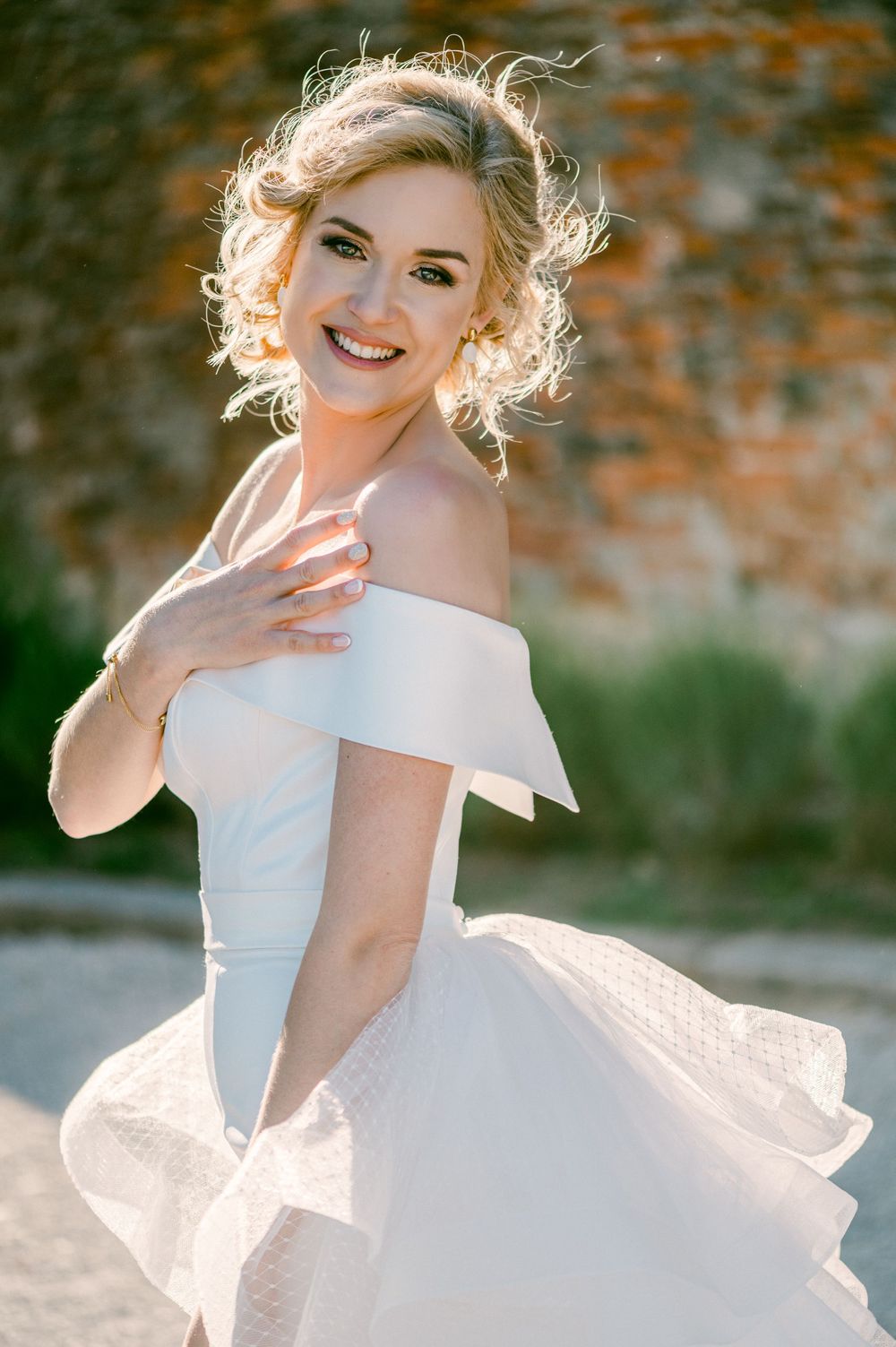 Ethereal bridal portrait showing an off-shoulder white wedding gown with flowing fabric backlit by soft natural light.