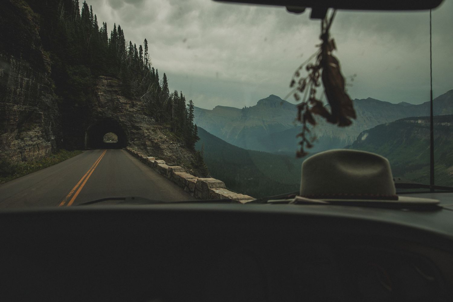 Mountain road view through car windshield with hat on dashboard and tunnel ahead.