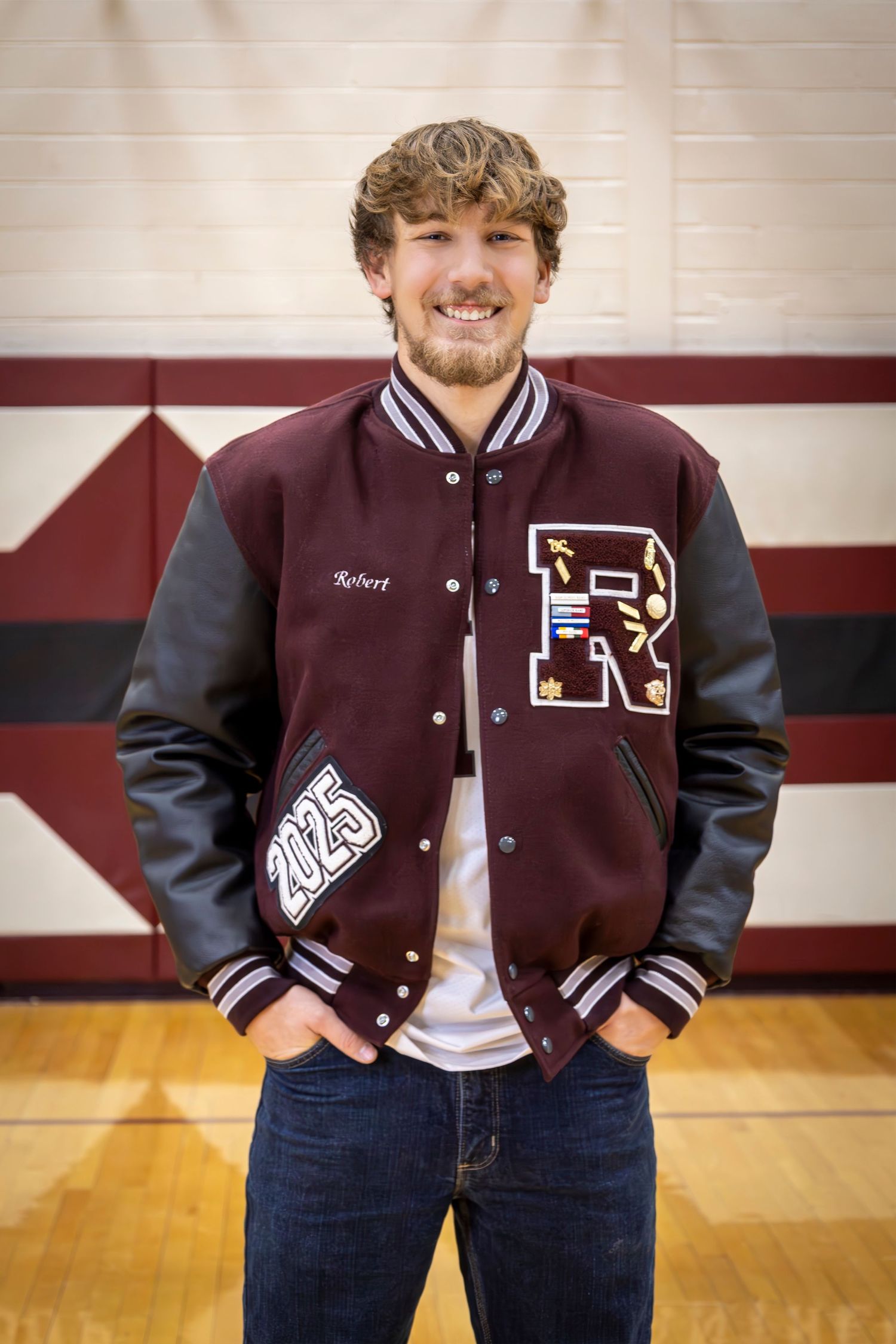 Senior boy having picture taken in high school gym with letterman jacket on.