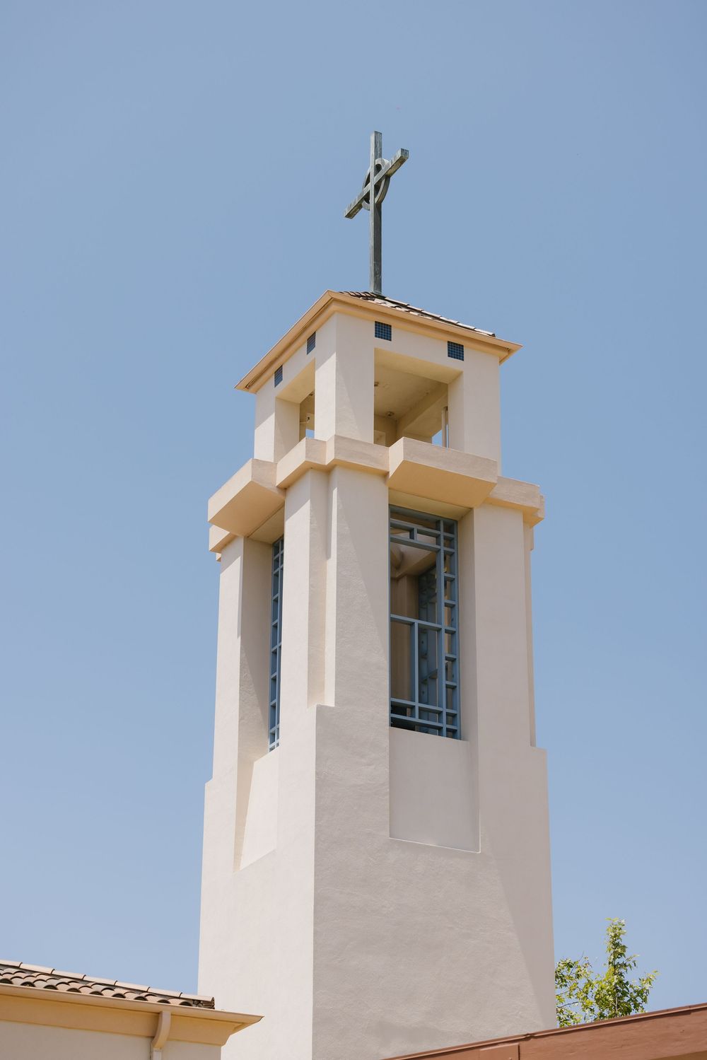 White stucco church bell tower with a cross on top against a clear blue sky.