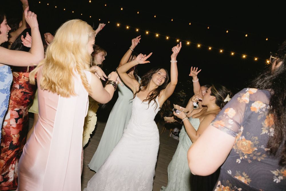 Guests dancing joyfully at an outdoor wedding reception under string lights at night.
