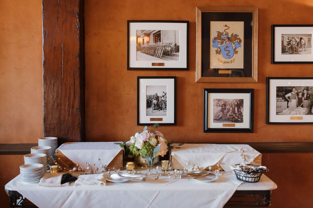 An elegant table setting with glassware beneath vintage framed photos on a terracotta-colored wall.