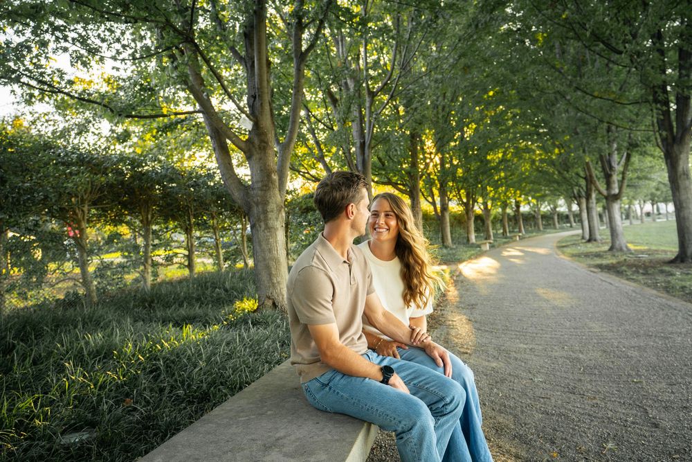 Couple sitting together on a park bench surrounded by trees during golden hour sunlight.