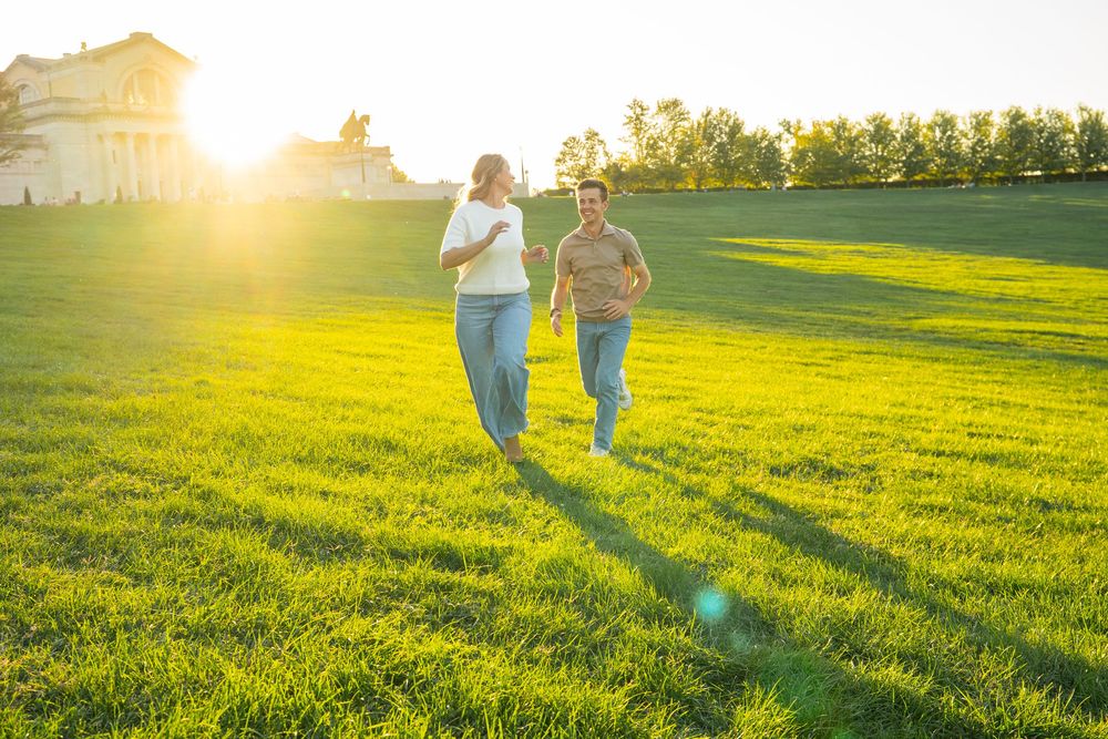 Two people walk together on a grassy hill at sunset casting long shadows across the golden meadow.