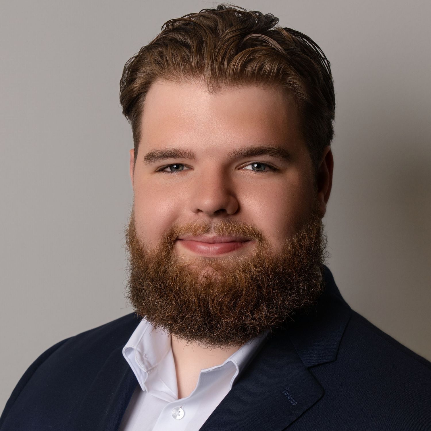 Professional headshot of person in navy suit and white shirt against neutral background with soft lighting.