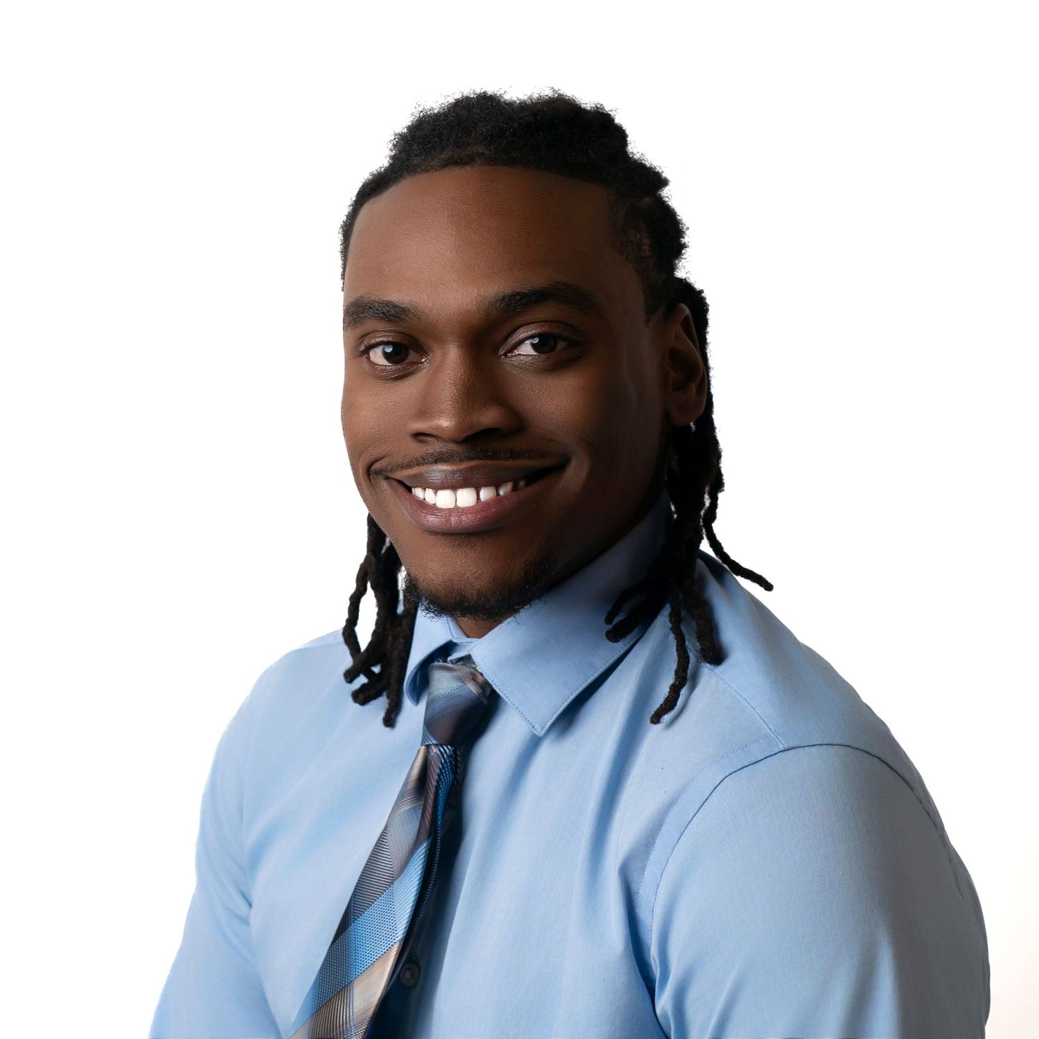 Professional headshot of a smiling person with dreadlocks wearing a light blue dress shirt and navy tie.