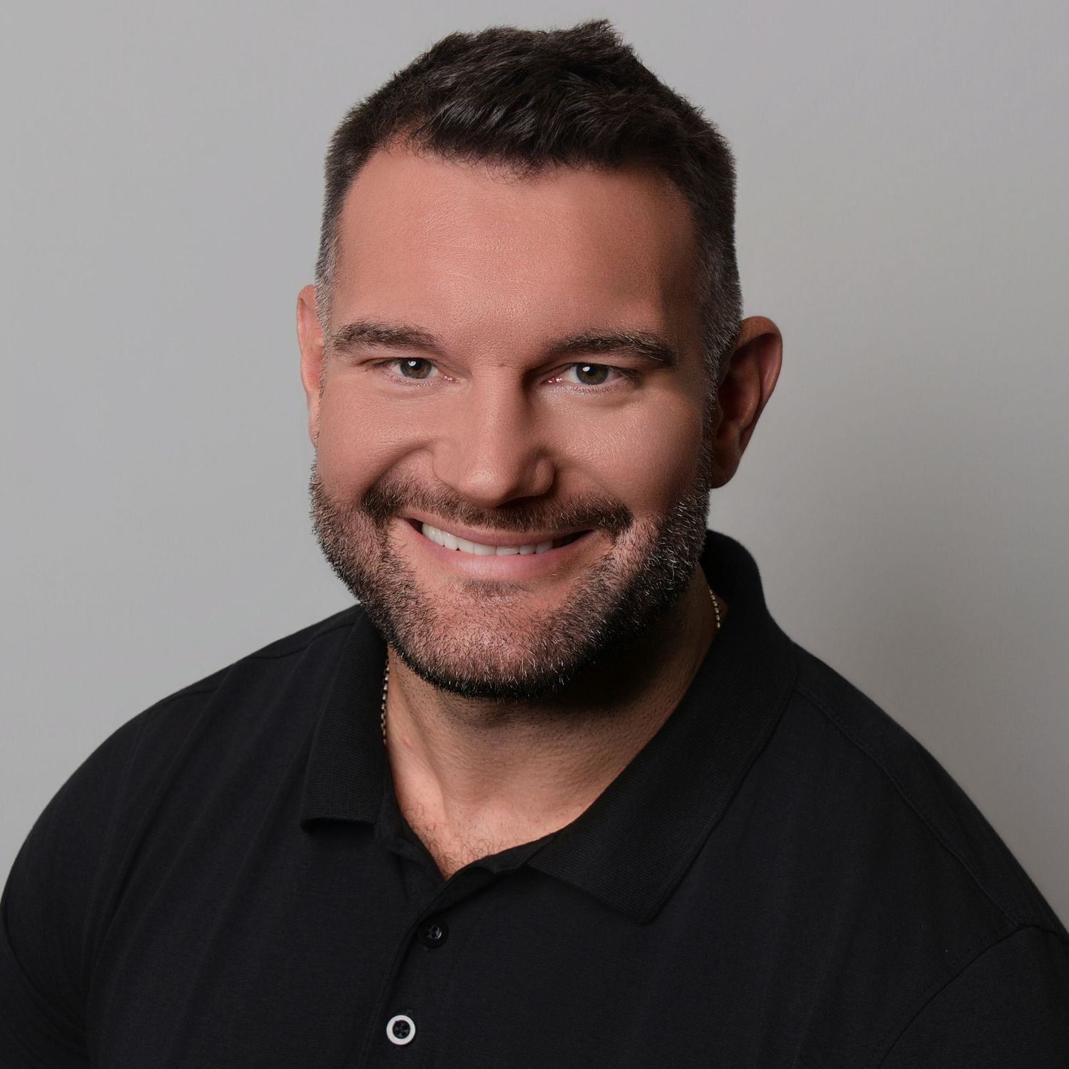 Professional headshot series of a person in a dark shirt against a gray background showing different expressions.