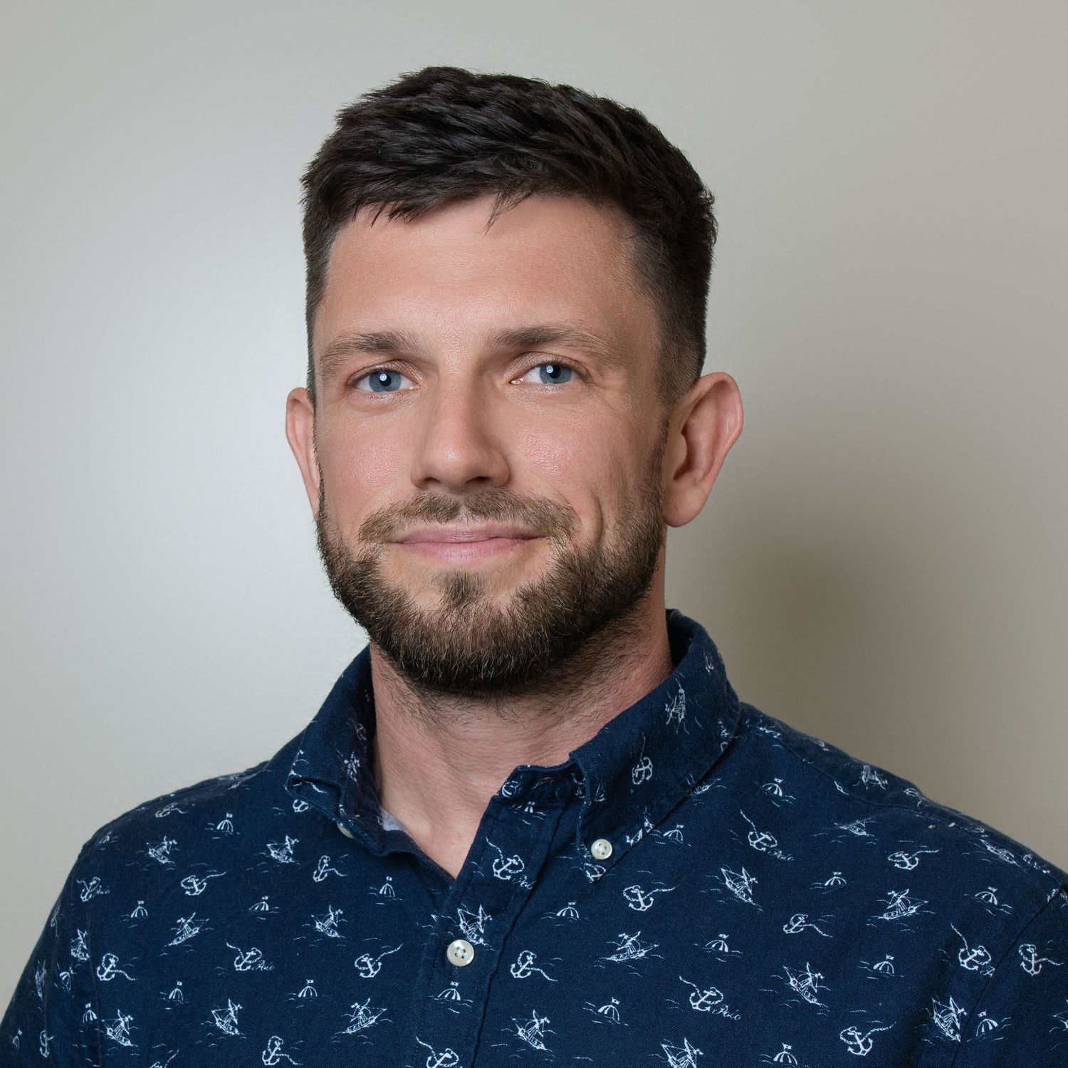 Professional headshot of a person wearing a dark patterned button-down shirt against a neutral background.