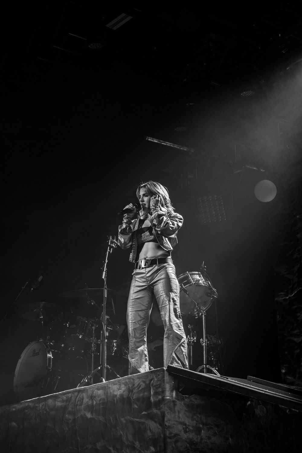 A dramatic black and white concert photo showing a performer on stage in silhouette against dramatic lighting.