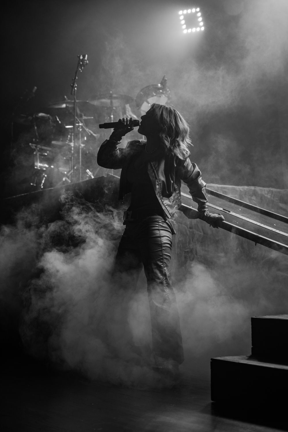 Atmospheric concert scene with fog and dramatic lighting showing a performer silhouetted on stage.