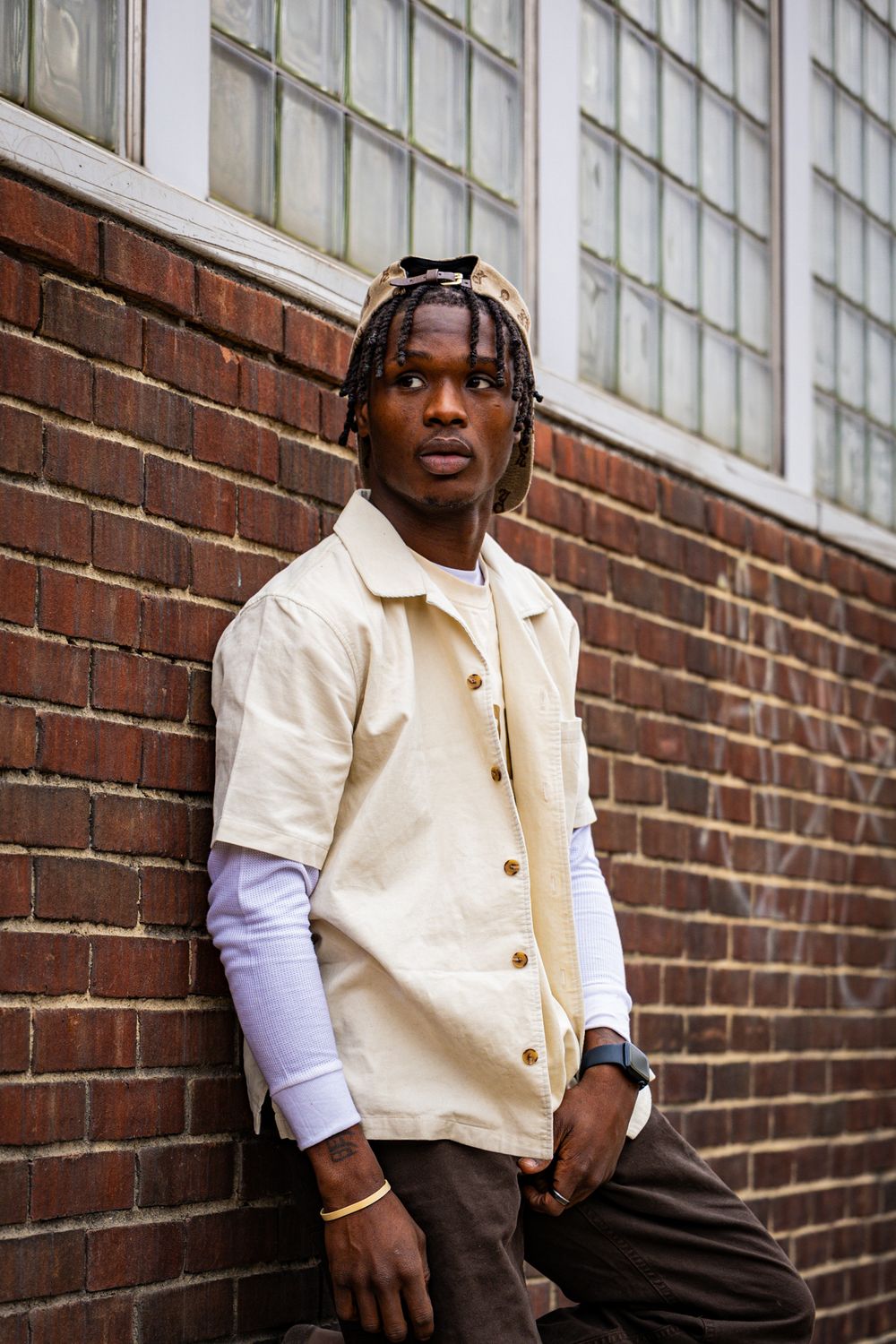 Stylish outfit featuring cream button-up jacket layered over purple long sleeve shirt against brick wall background.