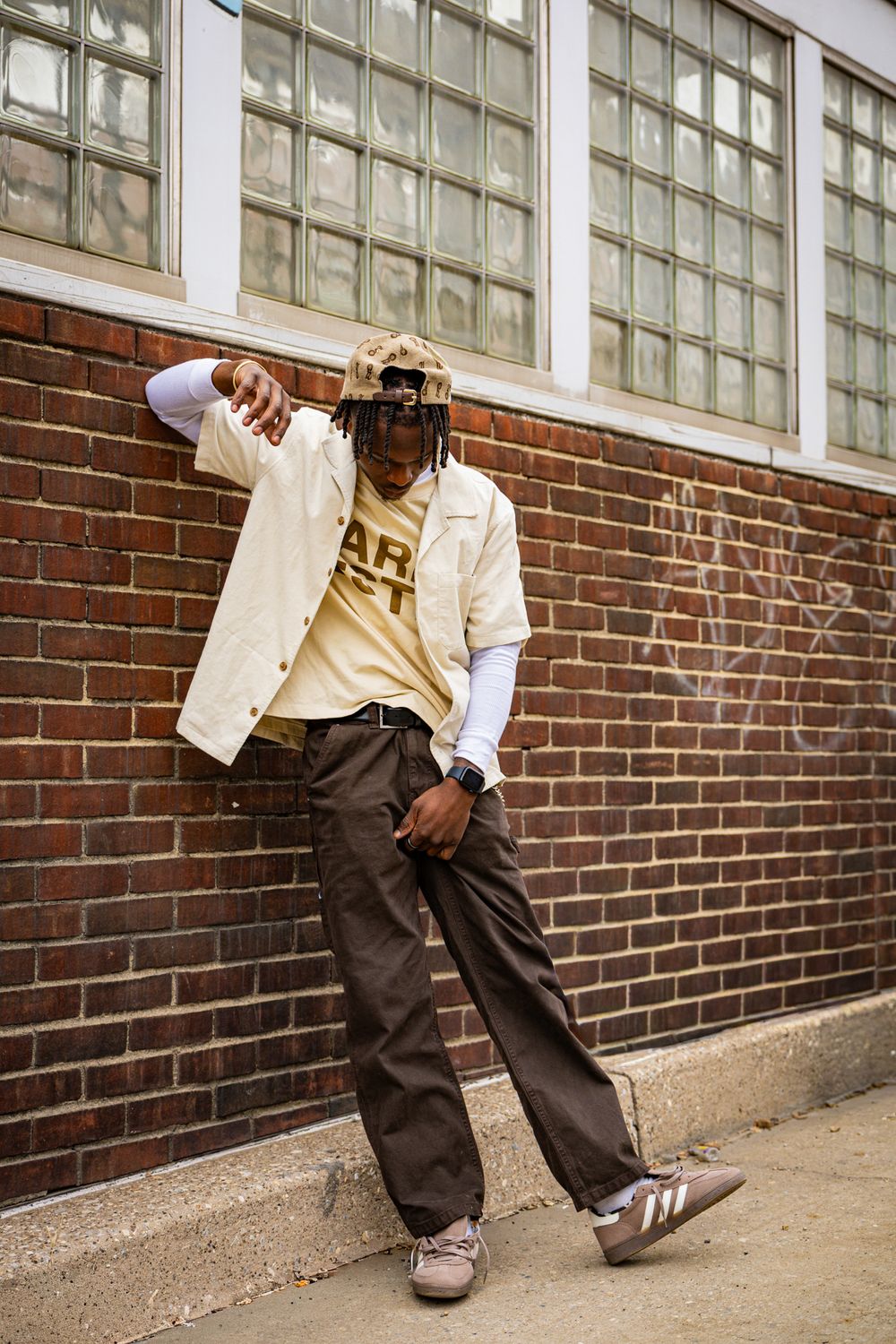 Four sequential photos showing someone in a white jacket and dark pants leaning against a brick wall in different poses.