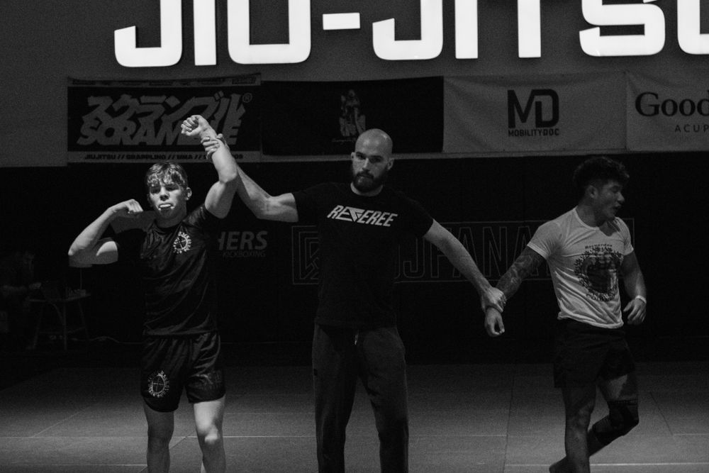 Two athletes demonstrate grappling techniques during a competitive jiu-jitsu match on the mat.