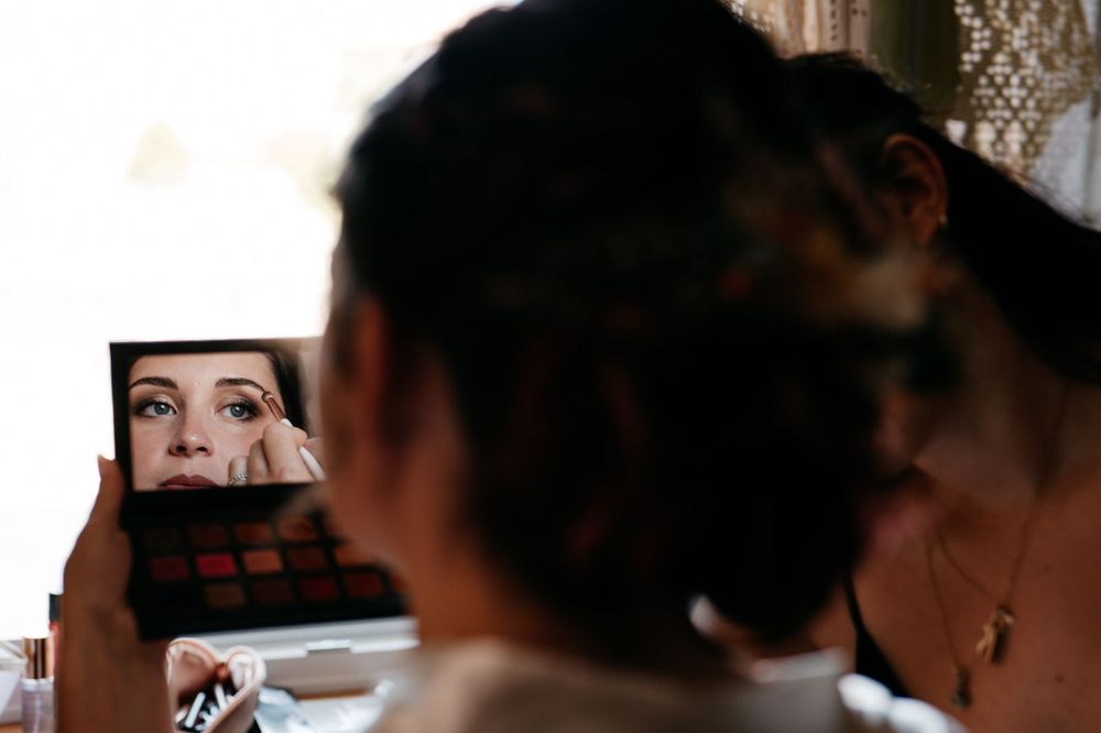 Someone applying makeup while looking in a small mirror.
