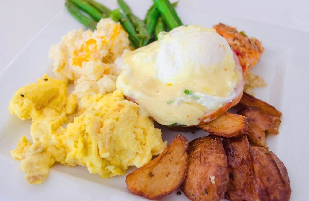 Classic breakfast plate with scrambled eggs, poached egg with hollandaise sauce, bacon and green beans on white plate.