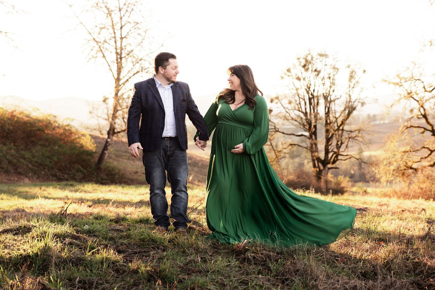 Two people in autumn field holding hands as emerald green dress flows dramatically in the breeze.